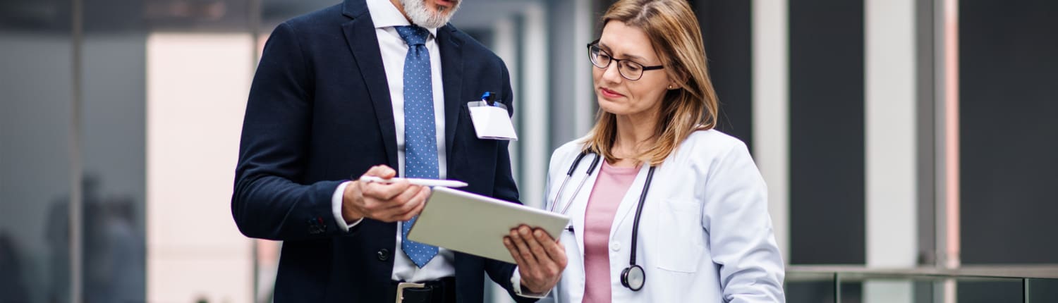 Pharmaceutical sales representative with tablet talking to doctor.
